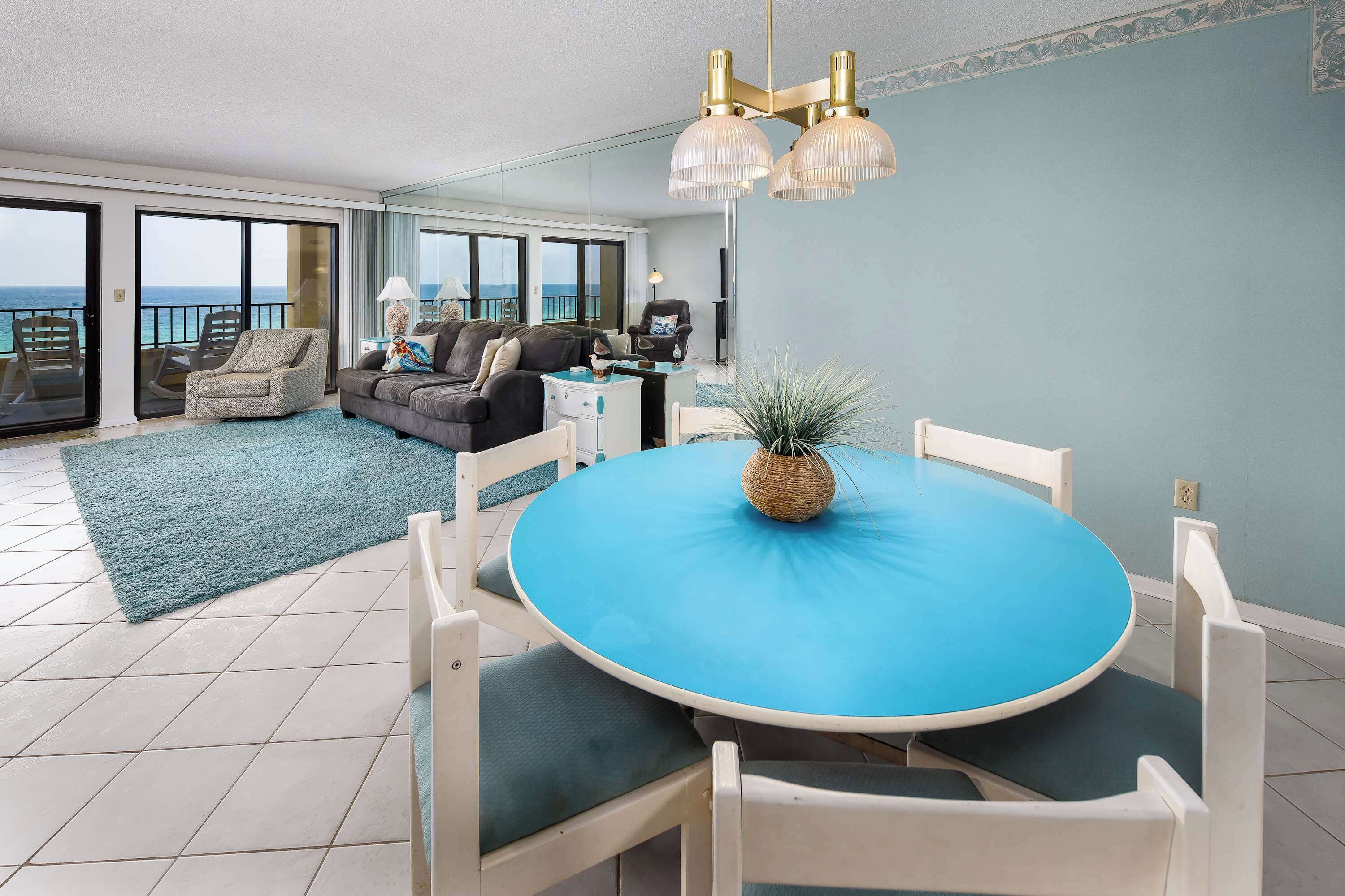 Un salón moderno con una mesa redonda, sillas blancas y vistas al mar a través de amplios ventanales correderas.