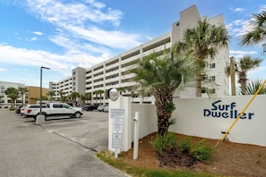 Un estacionamiento con un edificio blanco que dice 'Surf Dweller' y palmeras.