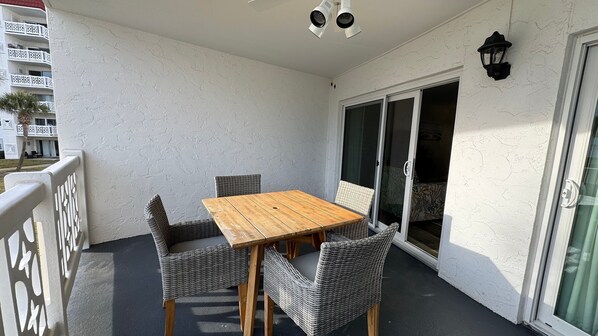 A balcony with a wooden table and wicker chairs, a sliding glass door, and a white textured wall.