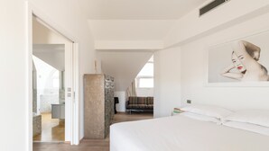 Ein modernes Hotelzimmer mit einem großen Bett, einer Wand mit Steinakzenten, einem Badezimmer mit Badewanne und Blick auf den Wohnbereich.
