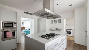 Eine moderne Küche mit Kochinsel, integriertem Backofen, Mikrowelle und einer Waschmaschine im angrenzenden Raum.