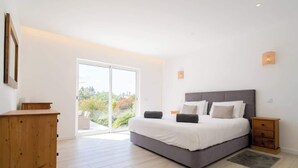 A bedroom with a large bed, a wooden dresser, a nightstand, and a sliding glass door leading to a balcony. - Spacious villa with pool, hot tub and large garden (Montinhos Da Luz)