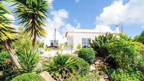 A modern house with a white exterior, surrounded by a lush garden with various plants and a clear blue sky. - Spacious villa with pool, hot tub and large garden (Montinhos Da Luz)