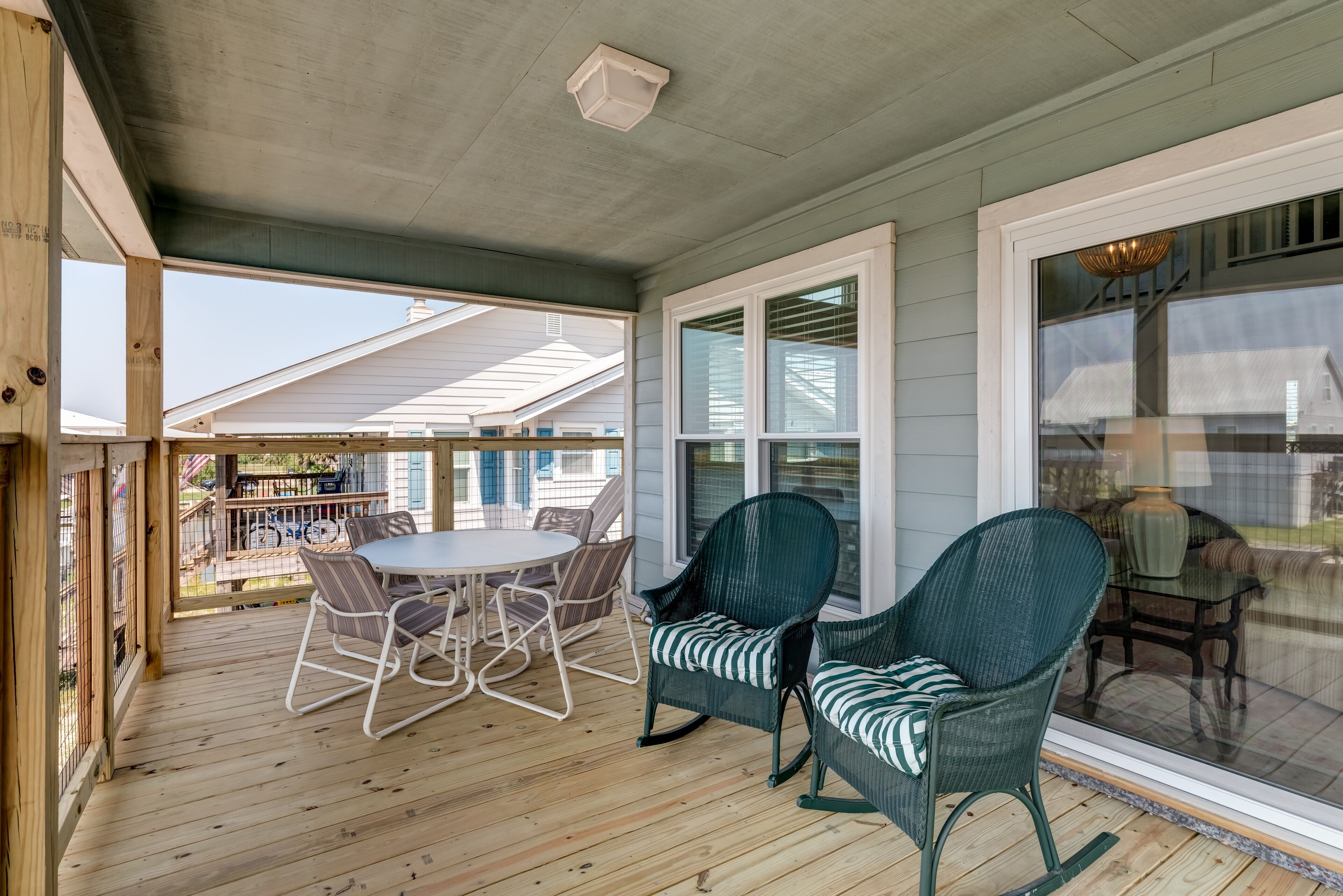 A covered porch with a round table and chairs, a rocking chair, and a glass door leading to a deck.