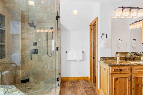 A modern bathroom with a glass-enclosed shower, wooden cabinets, and a granite countertop.