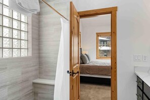 A bedroom with a wooden door, a window, a bed, and a bathroom with a shower curtain. - Waterdance House 4 Bedroom Home by RedAwning (Frisco)