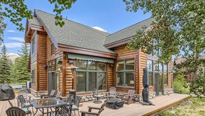 A log cabin with a deck, outdoor seating, and a large window overlooking a forested area.
