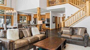 A spacious living area with a high ceiling, wooden staircase, and a kitchen with modern appliances.