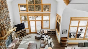 A spacious living room with a stone wall, large windows, a fireplace, and a television.