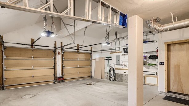 Eine Garage mit zwei großen Holztüren, einem Betonboden und einer Decke mit freiliegenden Balken und Leitungen.