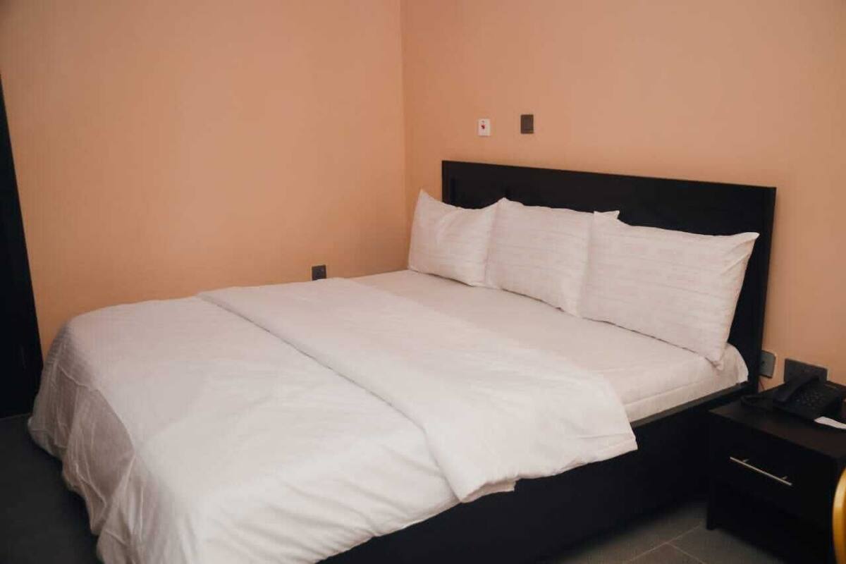A neatly made bed with white linens in a room with peach walls and a black headboard.