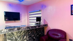 Un espace d’accueil moderne avec un comptoir en marbre, un téléviseur à écran plat et un fauteuil en cuir rouge.