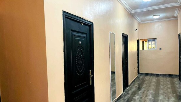 Un couloir aux murs de couleur beige, doté d’un plancher en bois et de portes noires.