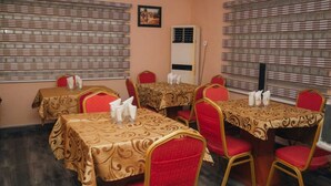 Une salle de conférence avec quatre tables, chacune recouverte d’une nappe à motifs et entourée de chaises rouges.