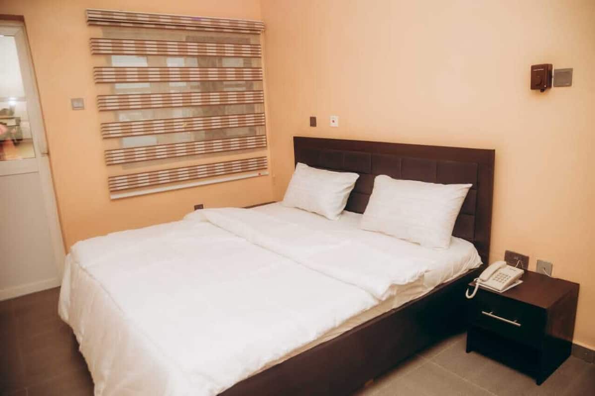 A neatly made bed with white linens, a dark wooden headboard, and a bedside table with a phone.