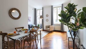 Un coin repas avec une table et des chaises en bois, un grand miroir rond et une grande plante en pot.