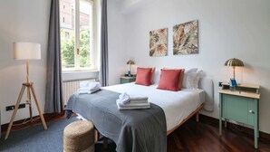 Une chambre d’hôtel avec un lit, deux tables de chevet, une lampe sur pied et des œuvres d’art accrochées au mur.