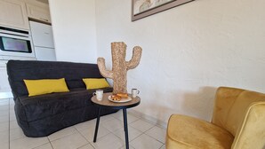 A modern living room with a dark grey sofa, yellow cushions, a small round table with a cactus decoration, a yellow armchair, and a Bosch refrigerator in the background.