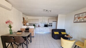 A modern kitchen with white cabinets, a dining area with a table and chairs, and a living area with a sofa and armchairs.