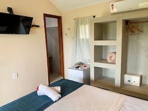 Habitació d'hotel amb llit, taula petita amb comandament a distància, mirall i armari amb barra penjant.
