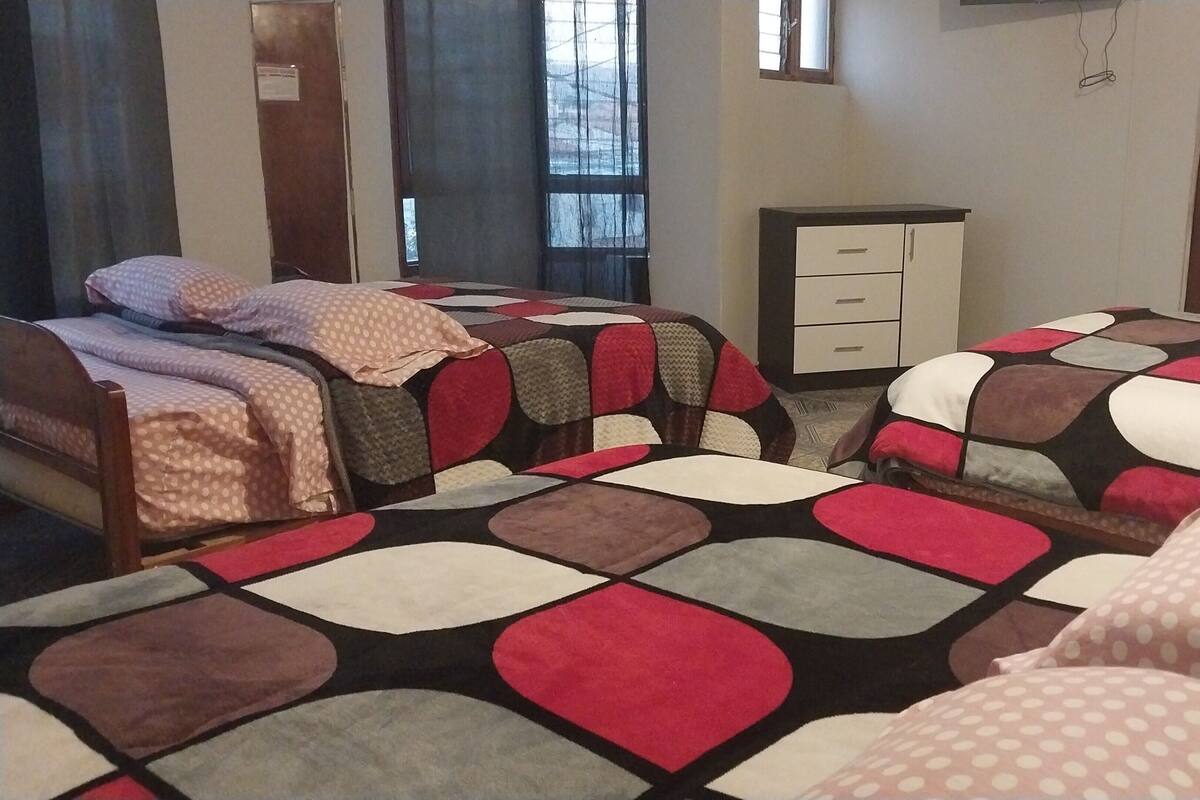 A room with two beds, each with a patterned bedspread, a small desk, and a window with curtains.