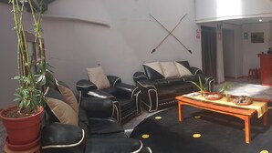 A living room with a sofa, armchairs, a coffee table, and a dining table. There is a potted plant, a striped chair, and a cabinet in the background. - Intipunku hospedaje (Cusco)
