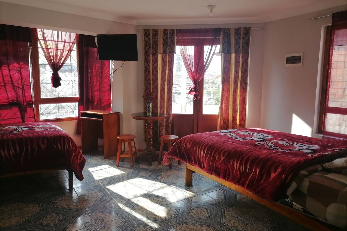 A room with two beds, a desk, a TV, and a window with curtains.