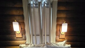 A bed with a white comforter and pillows, a dark throw blanket, and two wall-mounted lamps. - Martha's Place (Altura)