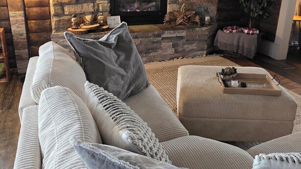 A cozy living room with a stone fireplace, a sofa with cushions, and a ceiling fan. - Martha's Place (Altura)