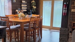 A dining area with a wooden table and chairs, a hanging light fixture, and a stone pillar. - Martha's Place (Altura)