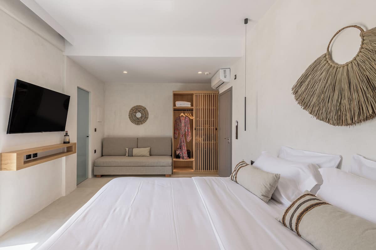 Un dormitorio moderno con una cama grande, un televisor montado en la pared, un armario y una zona de estar acogedora.