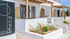 Een modern gebouw met twee verdiepingen, een witte gevel, houten pergola’s en een aangelegde tuin.