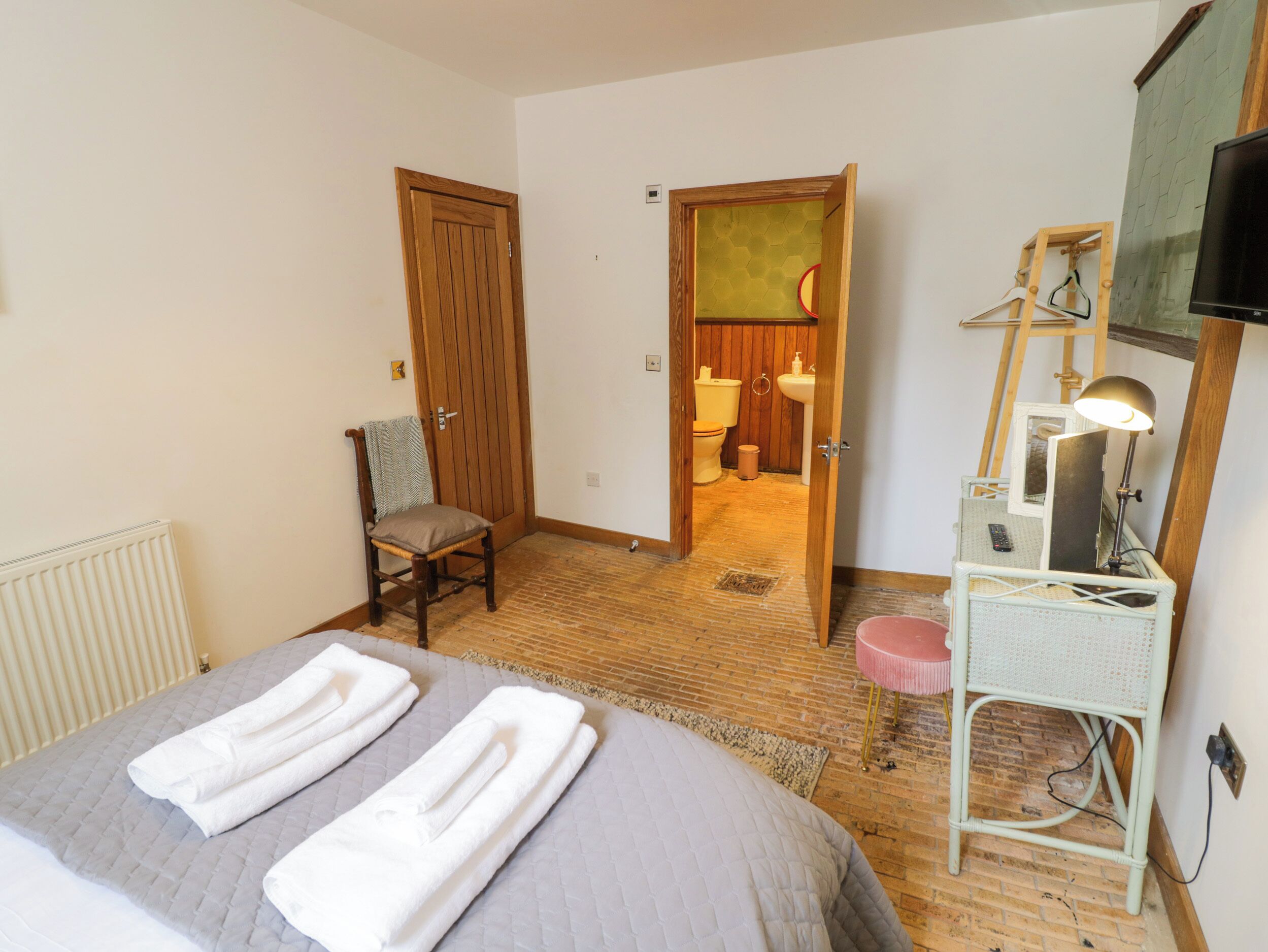Ein Hotelzimmer mit einem Bett, einem Sessel, einem Schreibtisch mit Lampe und einem durchgegangenen Tür angedeuteten Badezimmer.