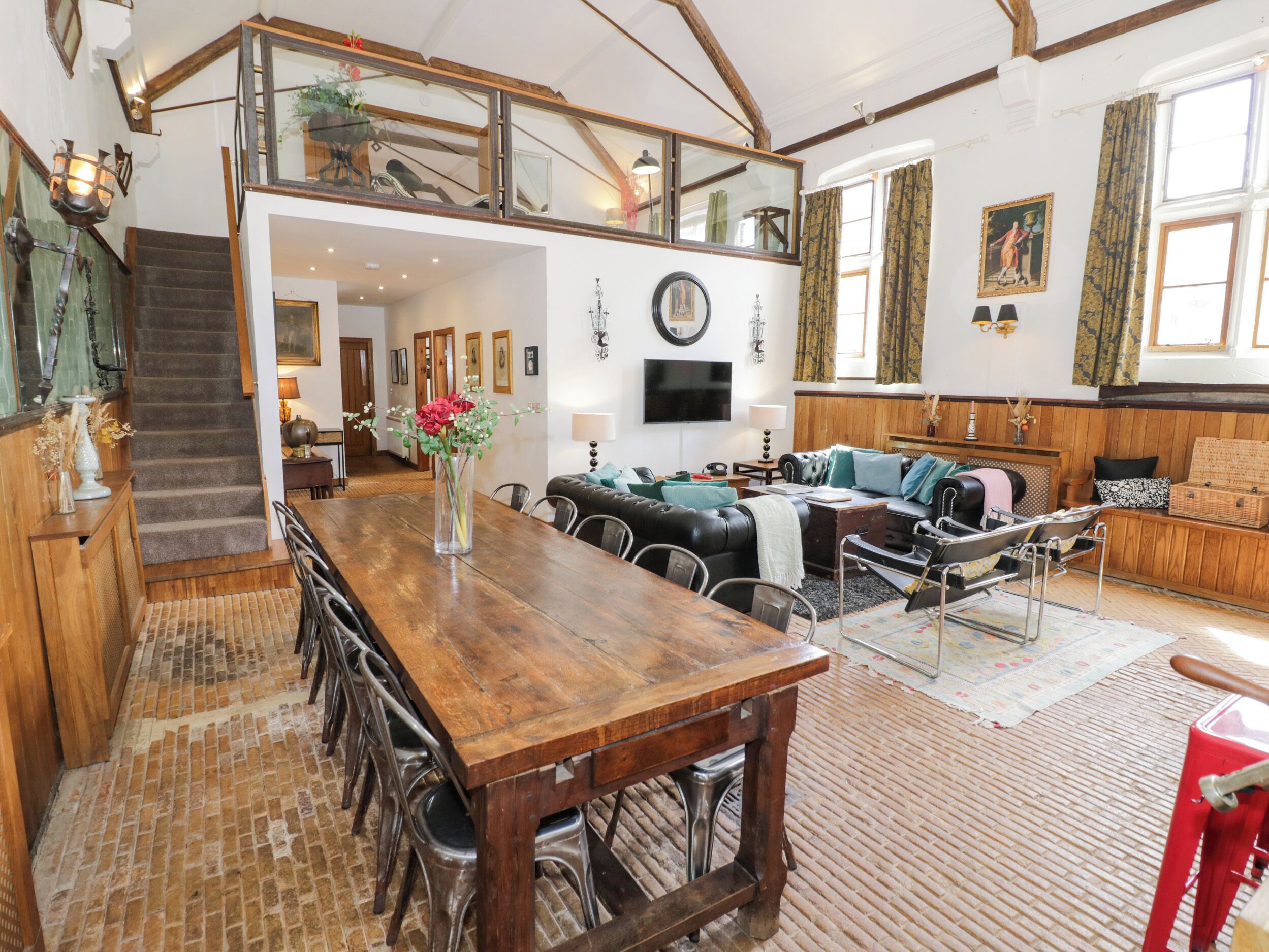A spacious living area with a wooden dining table, comfortable seating, and a staircase leading to an upper level.