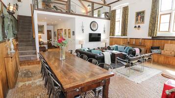 Un amplio salón con una mesa de comedor de madera, asientos cómodos y una escalera que sube a un nivel superior.