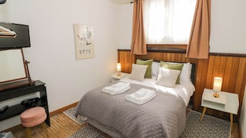 Quarto de hotel bem arrumado com cama, mesas de cabeceira, espelho, obra de arte na parede e um tapete estampado.