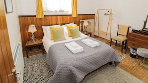 A hotel room with a bed, bedside tables, a chair, a wardrobe, a hanging clothes rack, and a window with curtains.