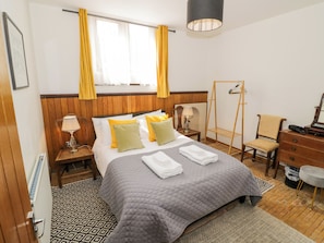 Una habitación de hotel con cama, mesitas de noche, una silla, armario, perchero y ventana con cortinas.