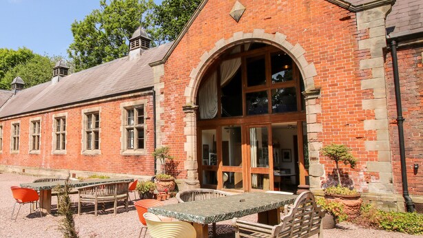 A traditional brick building with a large arched entrance, a gravel patio with a table and chairs, and a small garden area. - Talbot Lodge (Stafford)