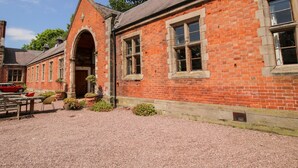 A red brick building with a gravel courtyard, a wooden bench, and a red car parked outside. - Talbot Lodge (Stafford)