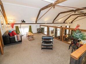 A spacious loft with high ceilings, exposed wooden beams, a leather sofa, a metal-framed chair, and a large window with curtains. - Talbot Lodge (Stafford)