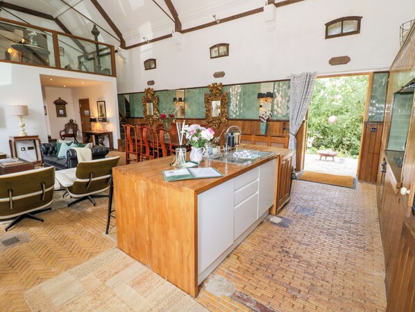 A spacious kitchen with a wooden island, a dining area with leather furniture, and a view of the outdoors. - Chetwynd Lodge (Stafford)