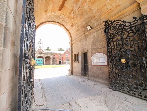 Una entrada con una gran y ornamentada puerta, un camino empedrado y un edificio con una torre de reloj al fondo.
