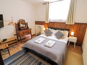 A hotel room with a bed, bedside table, lamp, mirror, and a hanging coat rack. - Chetwynd Lodge (Stafford)