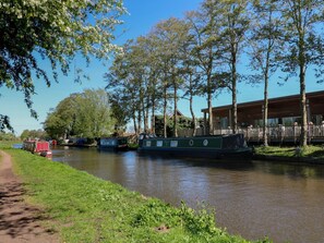 Un canal con barcos de recreo, un sendero cubierto de césped y un edificio de madera con terraza.