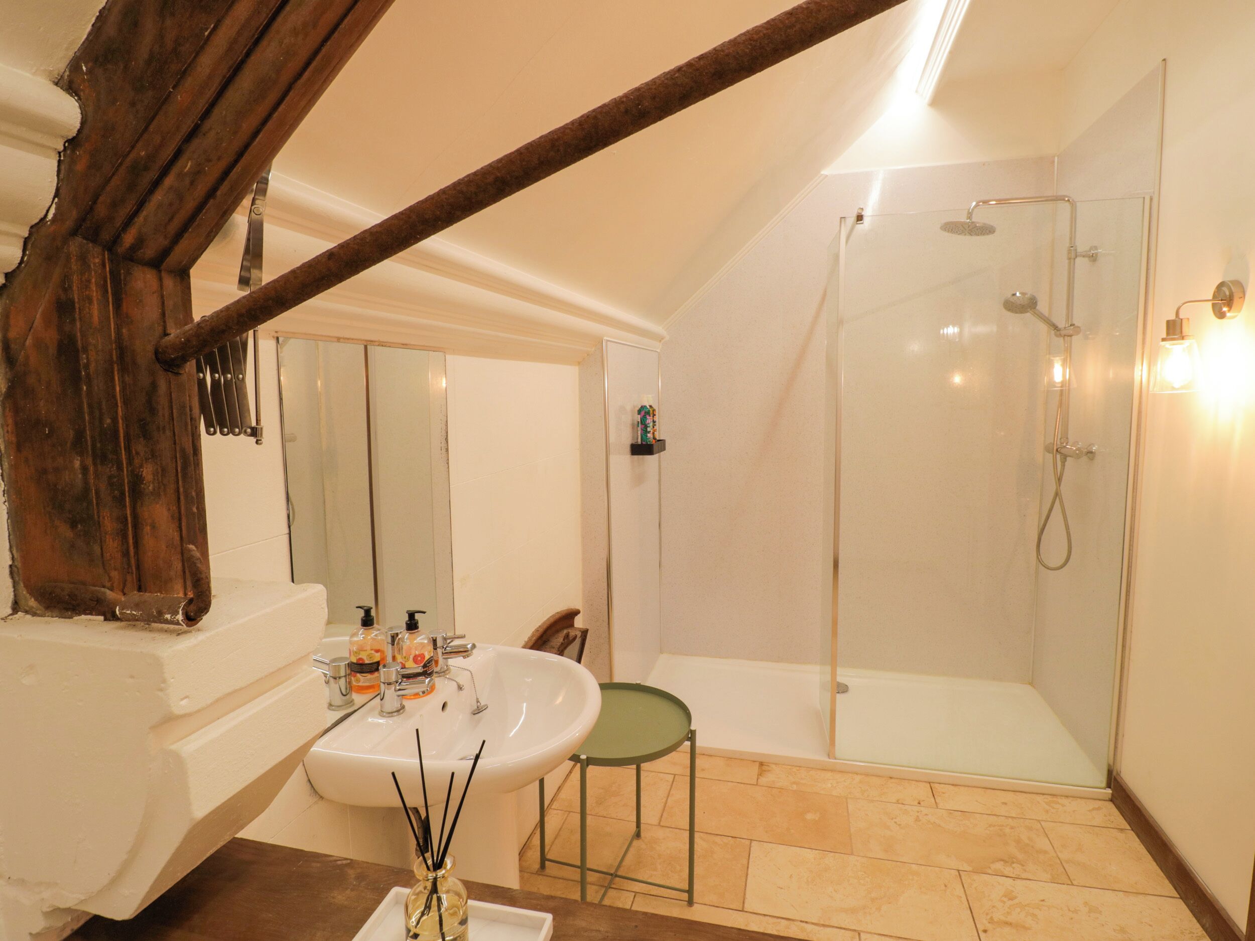 Un baño con ducha de vidrio, un lavabo con espejo y estructura de vigas de madera.