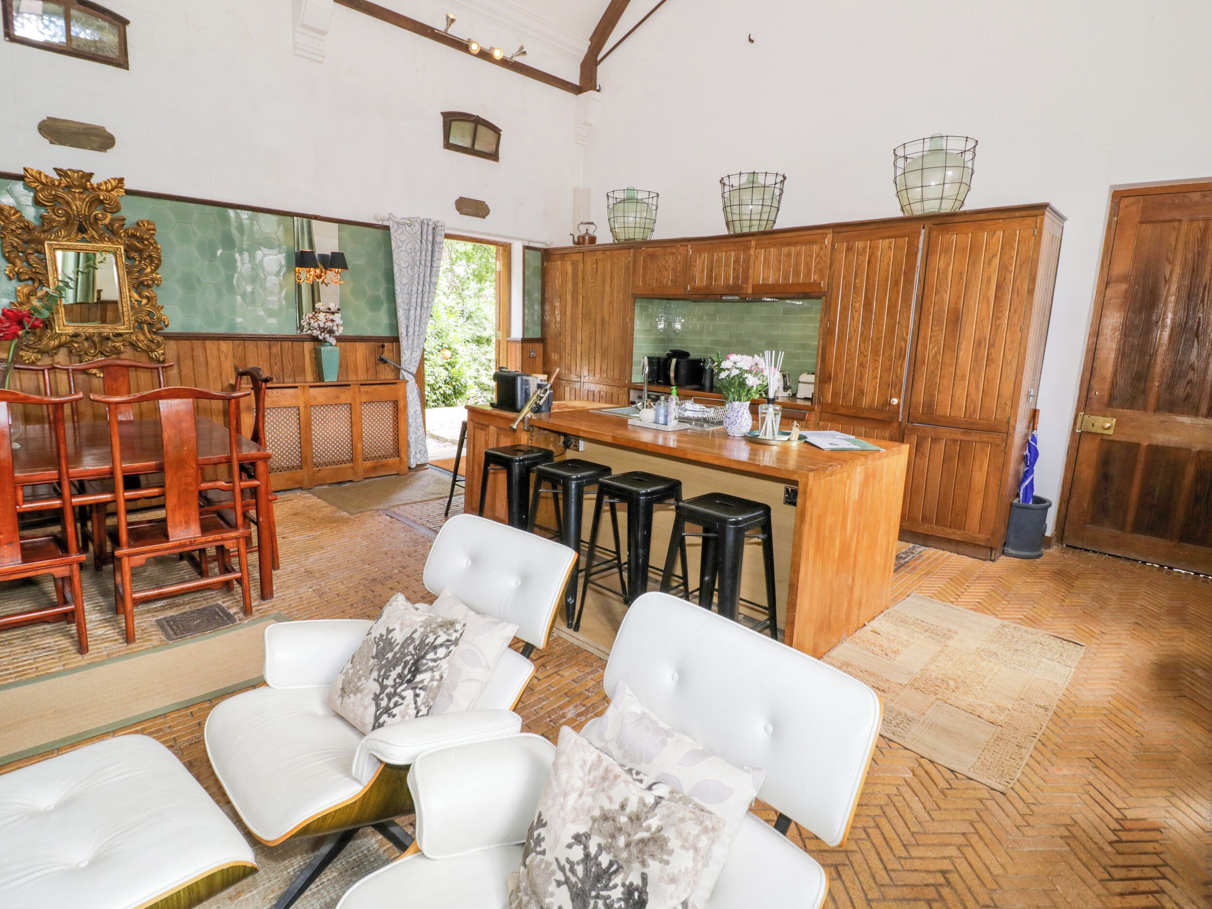Una cocina amplia con armarios de madera, una barra y un espacio de estar con sillas blancas.