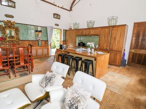 A spacious kitchen with wooden cabinets, a bar area, and a seating area with white chairs. - Chetwynd Lodge (Stafford)