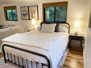 Quarto bem arrumado com uma cama, duas mesas de cabeceira com abajures, um radiador e quadros nas paredes.