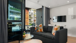 Uma sala de estar moderna com um sofá, uma mesa de centro e vista para um edifício com áreas verdes.
